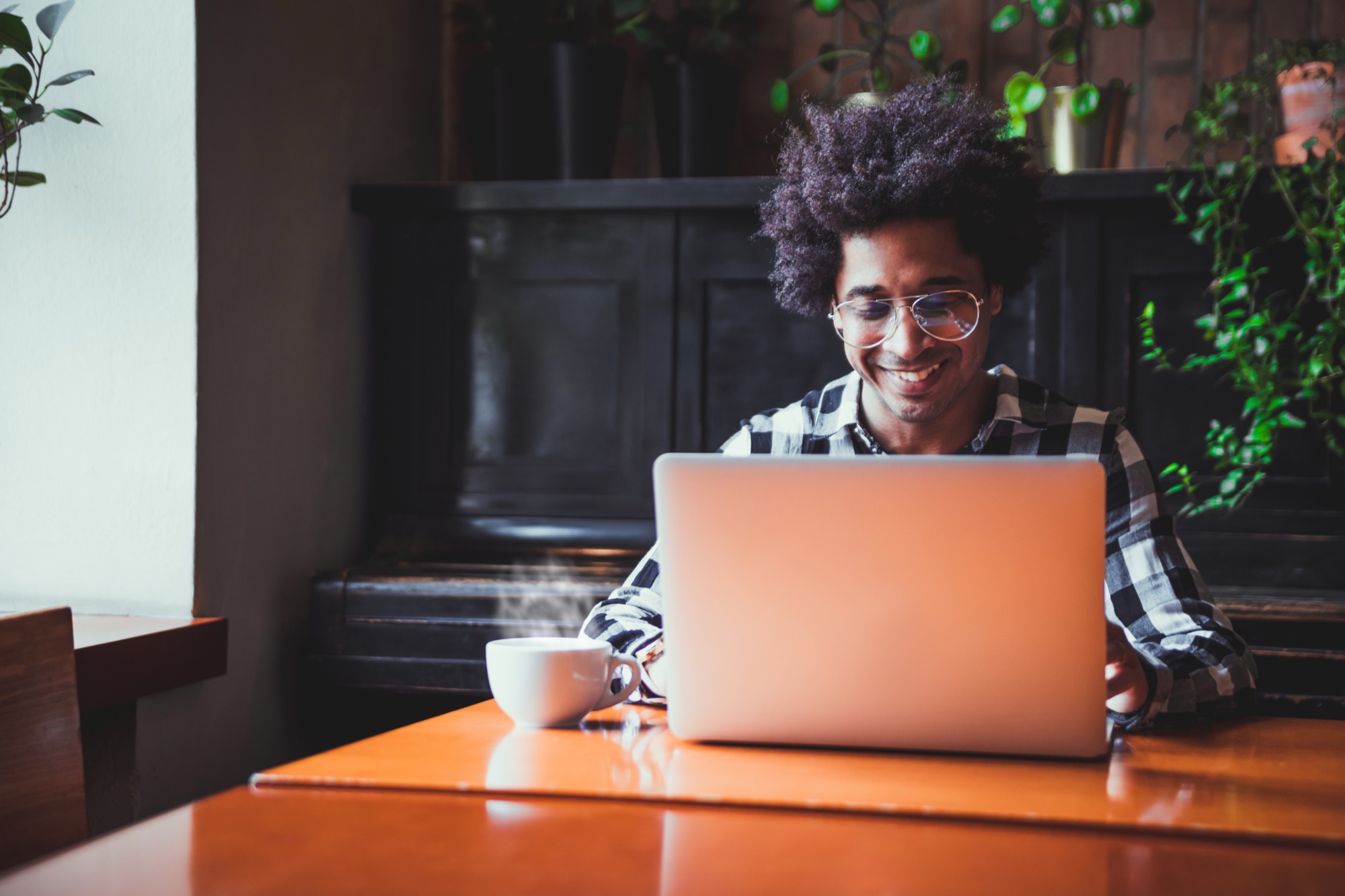 A young writer smiling at a laptop over coffee, carrying Ida B. Wells' pen forward